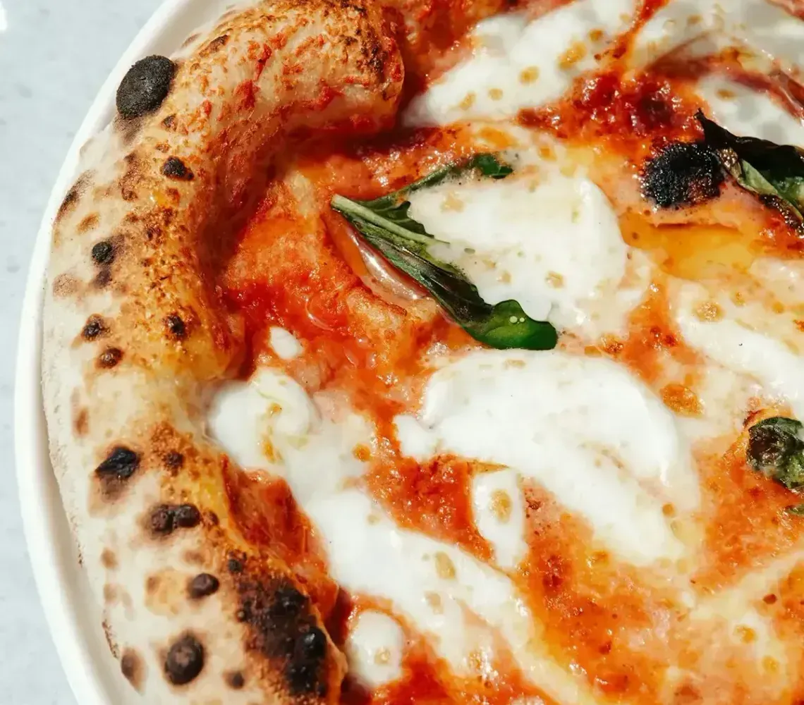 Close-up of a margherita pizza with melted mozzarella, tomato sauce, and basil on a plate