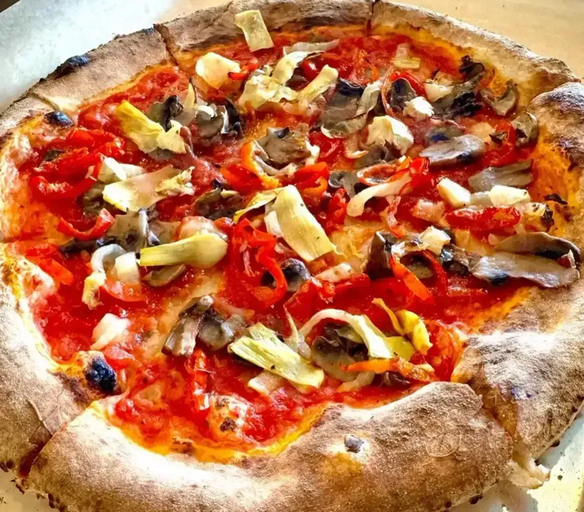A partially eaten mushroom and tomato pizza on a metal tray, with a golden-brown crust.