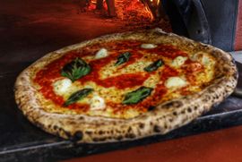 Neapolitan pizza with basil and mozzarella baking in a wood-fired oven