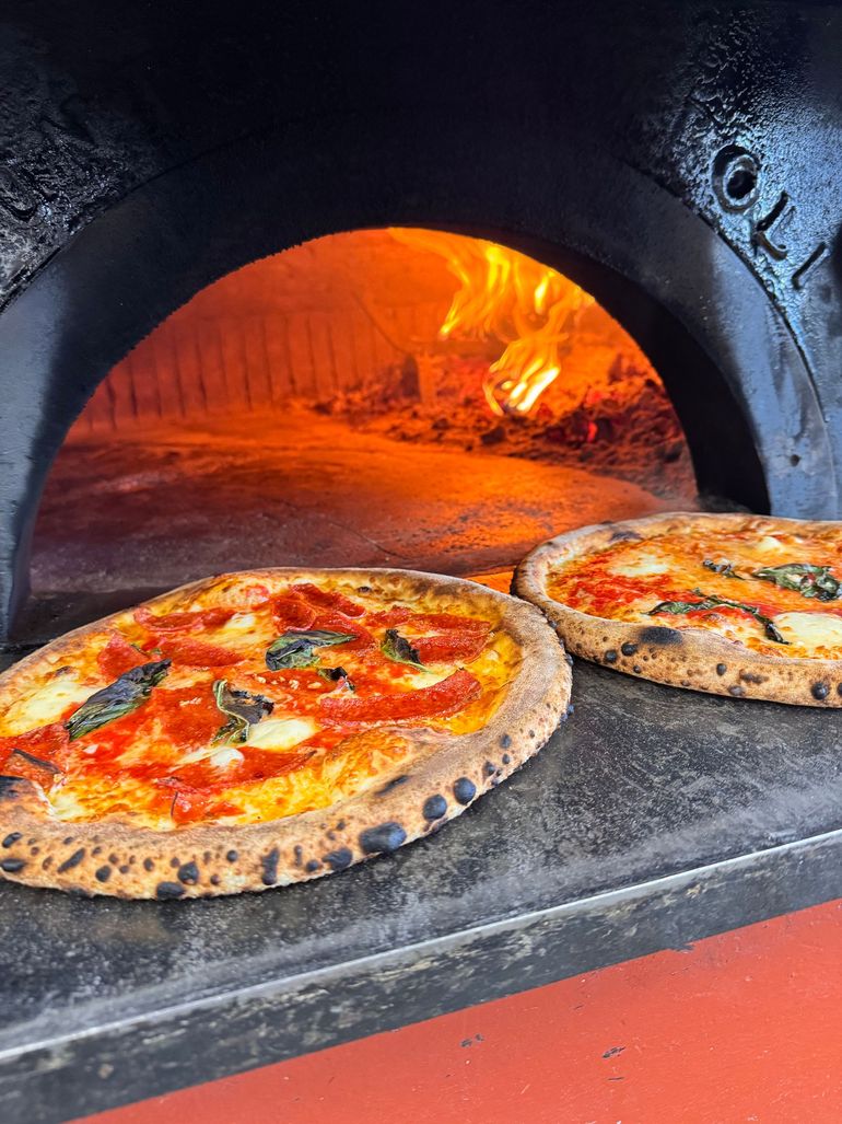 Wood-fired pizza topped with tomatoes, melted cheese, and arugula on a wooden board