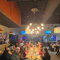 Crowded restaurant with diners at long tables under warm pendant lights and exposed ductwork