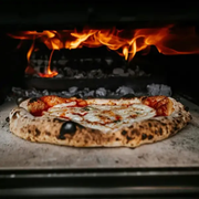 Pizza baking in a wood-fired oven with flames above the crust
