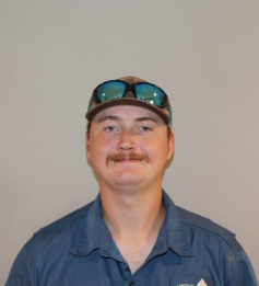 Person in a blue shirt and cap with reflective sunglasses resting on the brim, facing forward and smiling.