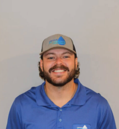 Smiling man in a blue polo and gray cap standing against a plain background