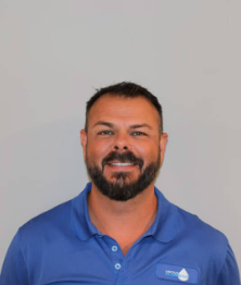 Smiling man with beard in a blue polo shirt against a plain gray background