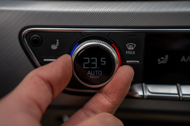 Die manuelle Einstellung eines Drehreglers der Autoklimaanlage, der 23,5 °C auf dem Armaturenbrett anzeigt.
