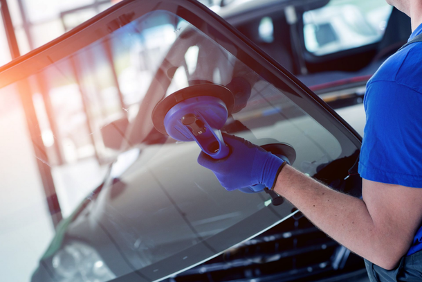 Eine Person, die in einer Garage eine Autoscheibe mit einem Tuch poliert, trägt blaue Handschuhe und ein blaues Hemd.
