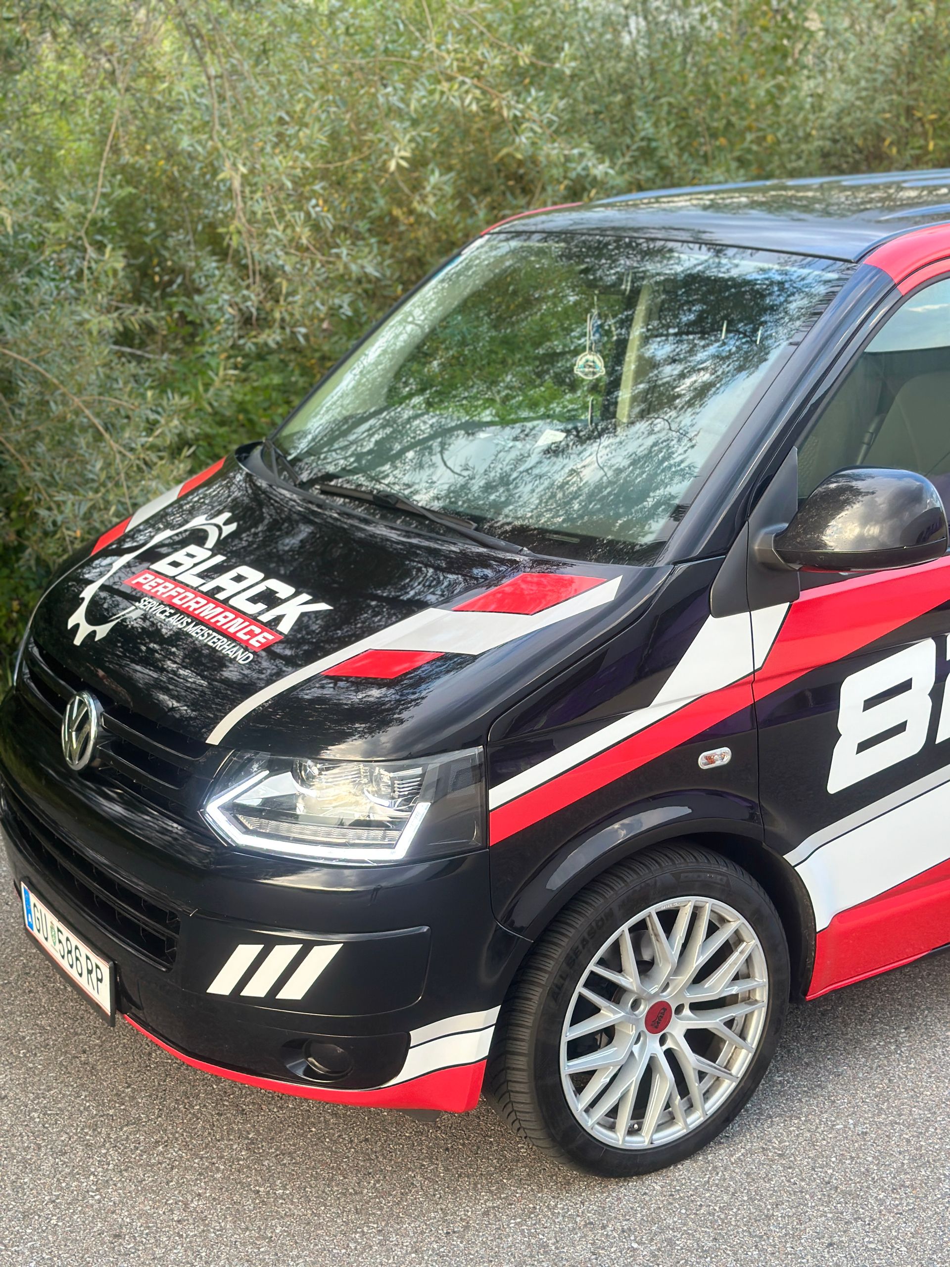 Schwarzer Rallyewagen mit rot-weißen Rennstreifen parkt neben Büschen.