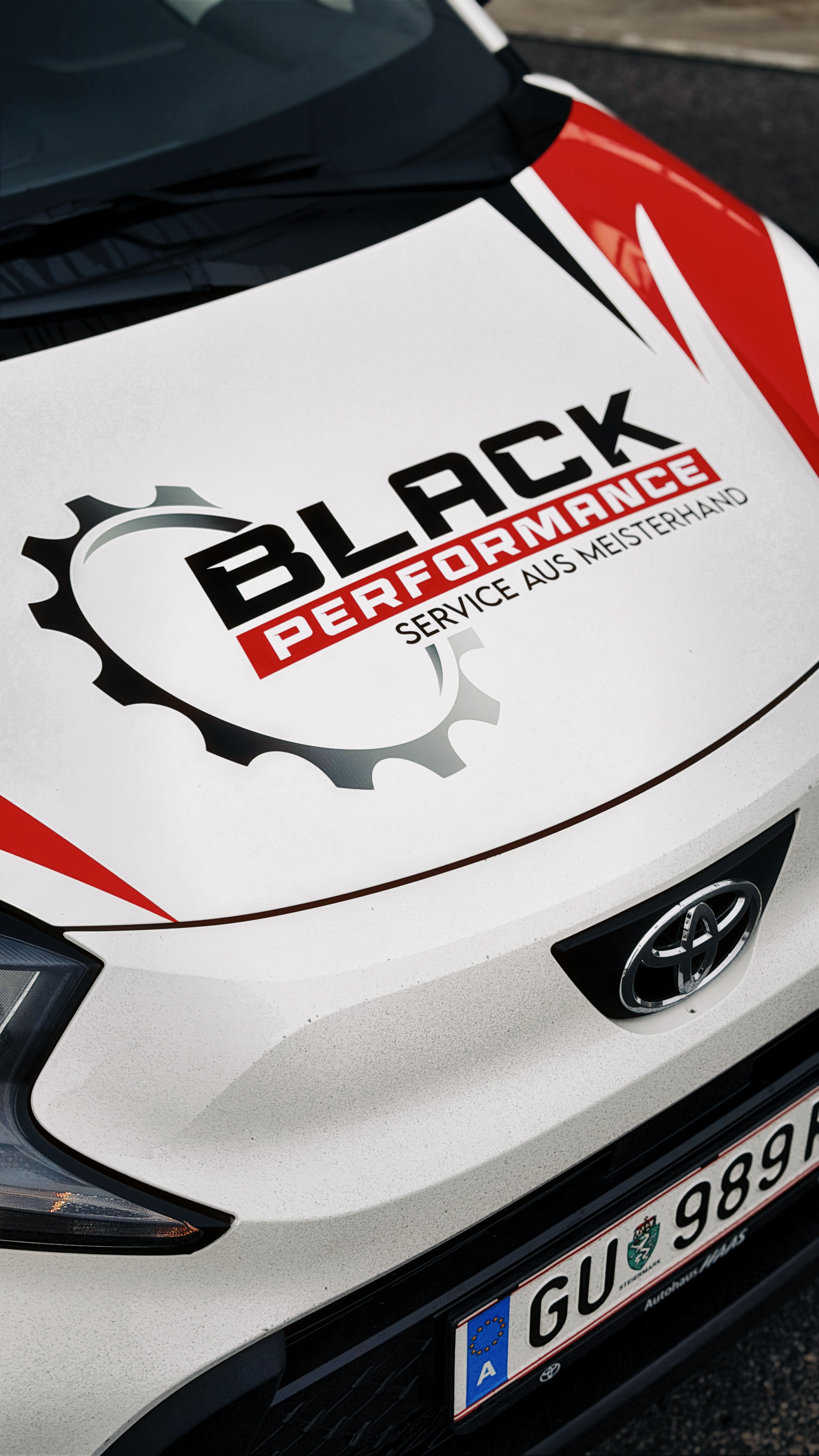 Nahaufnahme einer weißen Motorhaube mit roten Akzenten und einem „Black Performance“-Aufkleber