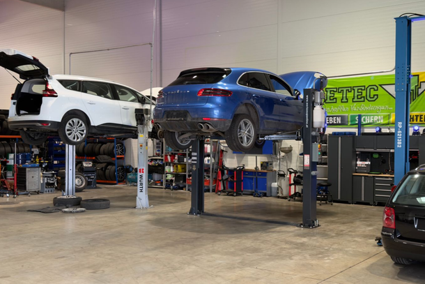 Zwei Autos, eines weiß und eines blau, wurden in einer Autowerkstatt auf Hebebühnen angehoben.