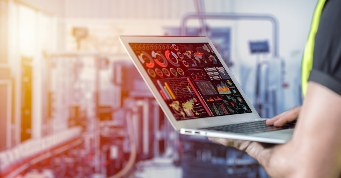 Pessoa utilizando um laptop em um ambiente industrial, visualizando um painel com gráficos e controles de dados em vermelho.
