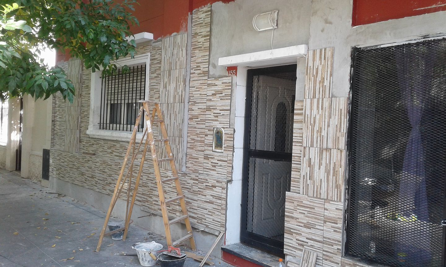 Pequeño local comercial con fachada de piedra, puerta y ventana negras, y una escalera de bambú en la acera.