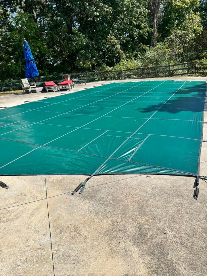 Green pool cover stretched over a rectangular pool on a concrete patio.