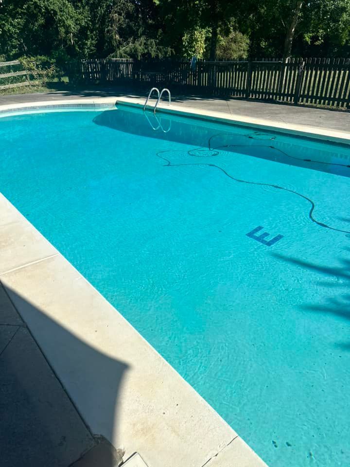 A rectangular outdoor swimming pool filled with turquoise water, a ladder, and a dark hose.