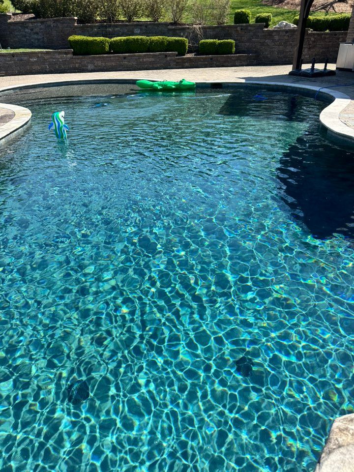 Blue swimming pool with light reflections, floaties, and a stone patio.