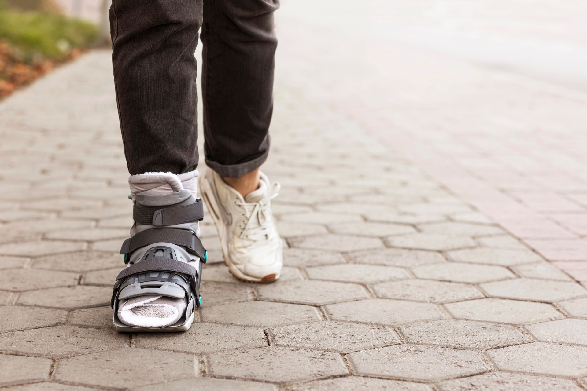 Una persona cammina su un sentiero lastricato indossando uno stivale ortopedico su un piede e una scarpa da ginnastica bianca sull'altro.