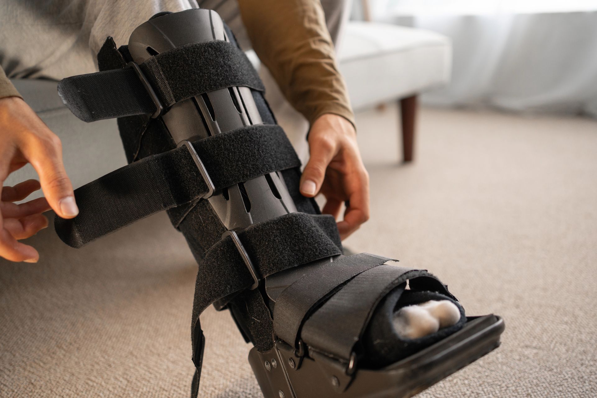 Una persona seduta regola le cinghie in velcro di uno stivale ortopedico nero indossato sulla parte inferiore della gamba.