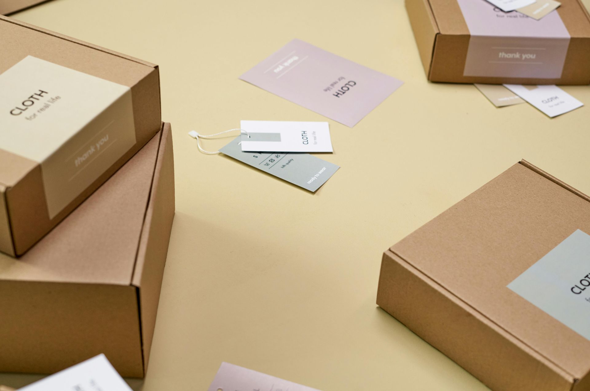 Caixas de papelão com etiquetas e cartões de agradecimento em uma superfície amarelo claro.