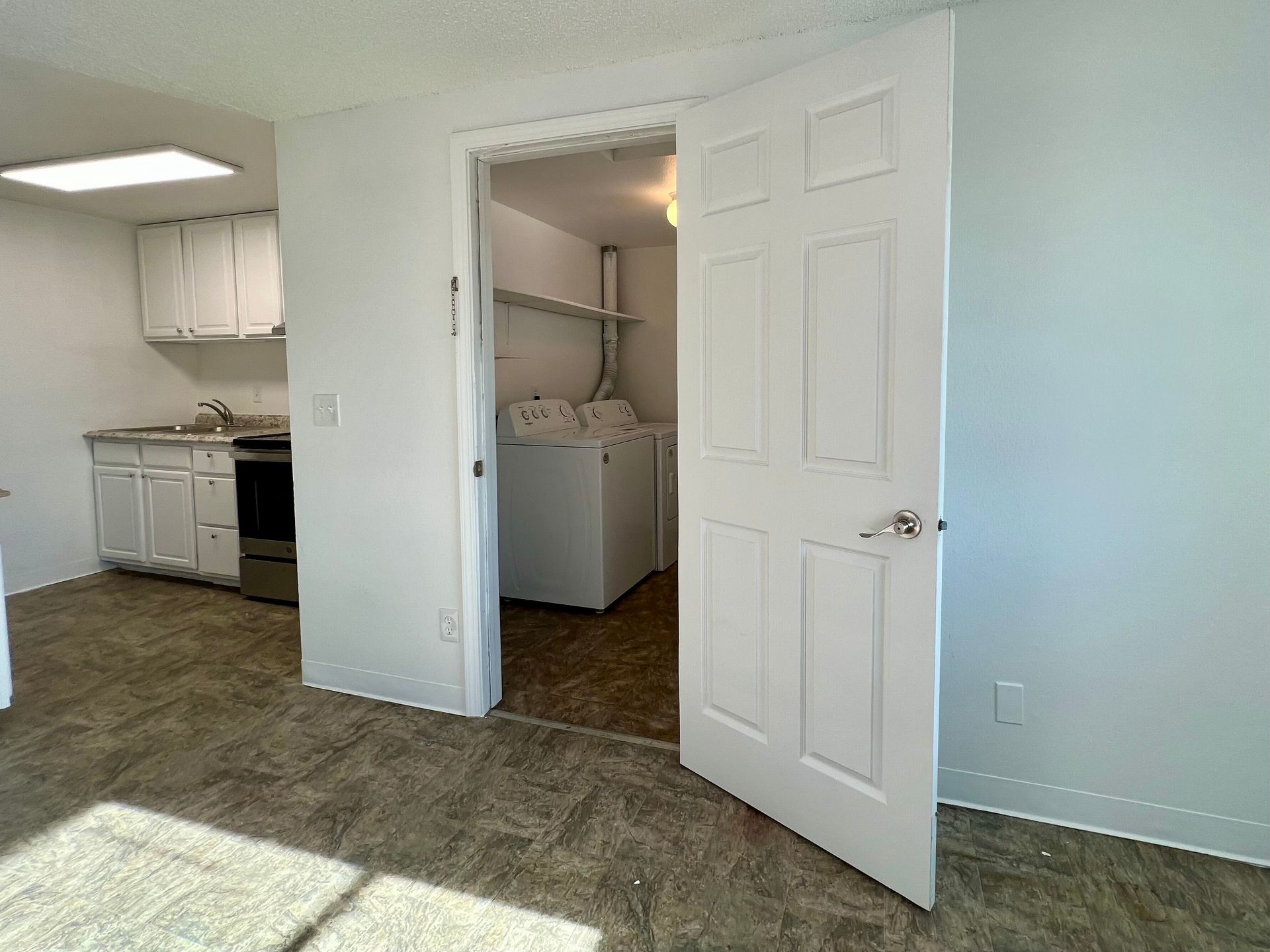 Empty apartment interior with carpet, white walls, open doors, and a laundry area visible.