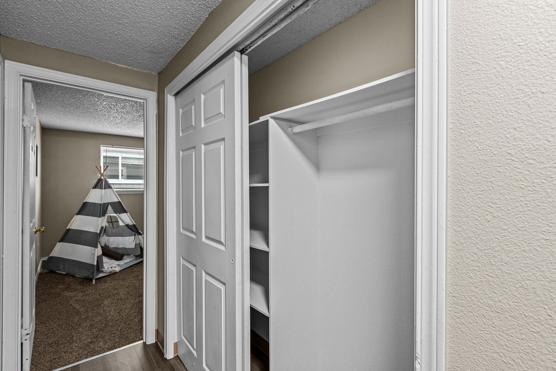Empty hallway with open closet doors and a teepee visible in the adjacent room.