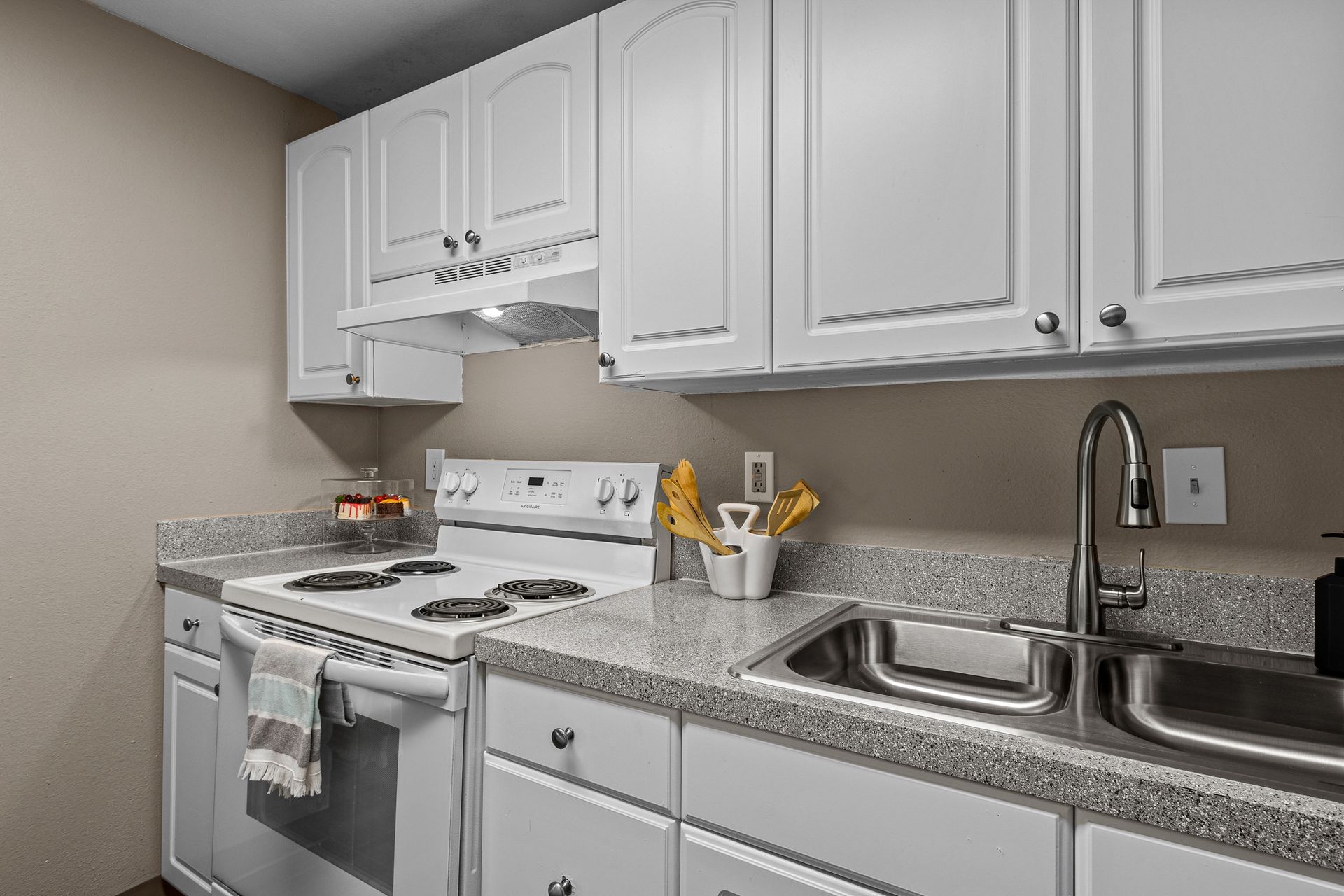 Bright kitchen with white cabinets, granite counters, gas stove, and stainless steel sink.