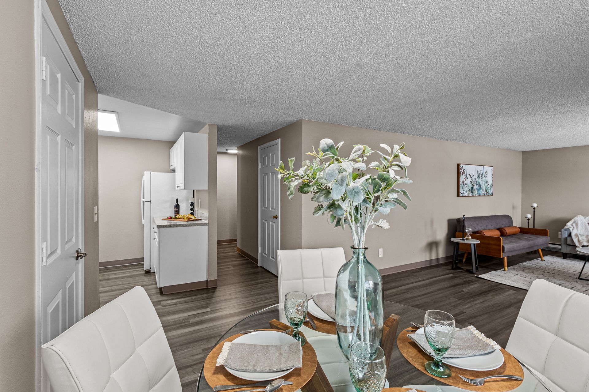Modern apartment dining area with set table, white chairs, and a living room in the background