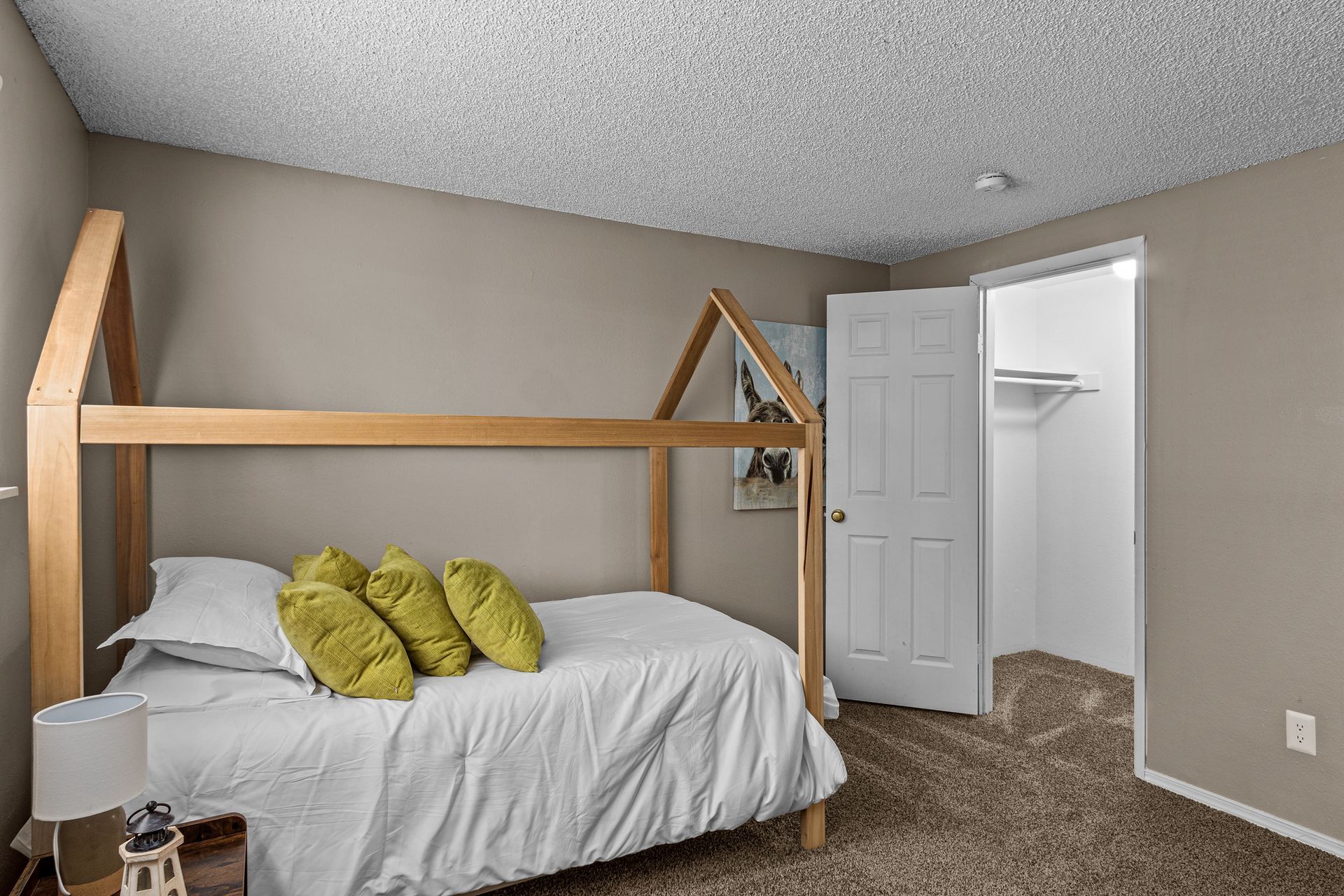 Cozy bedroom with a wooden bed frame, white bedding, green pillows, open closet, and gray carpet.