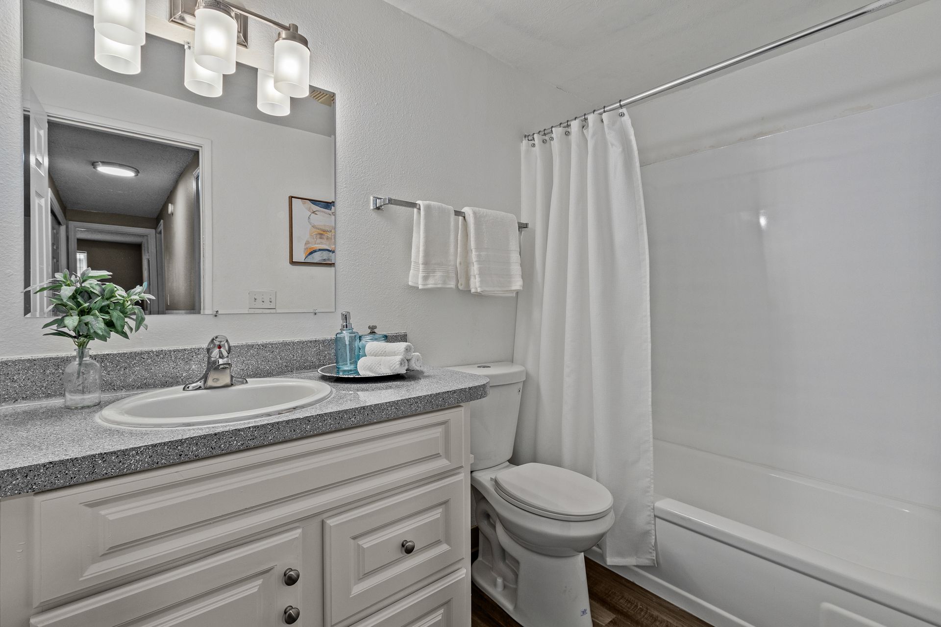 Bright bathroom with vanity, mirror lights, toilet, and white shower curtain