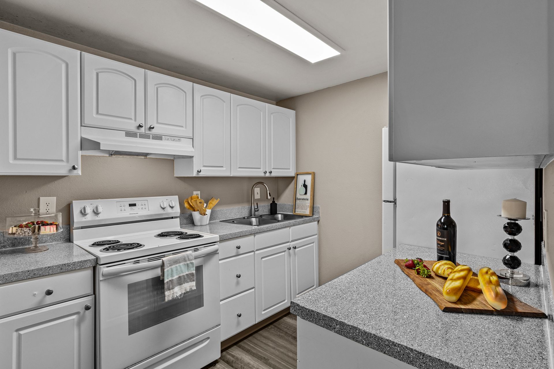 Bright white kitchen with stove, cabinets, granite counters, and a bowl of bananas on the island.