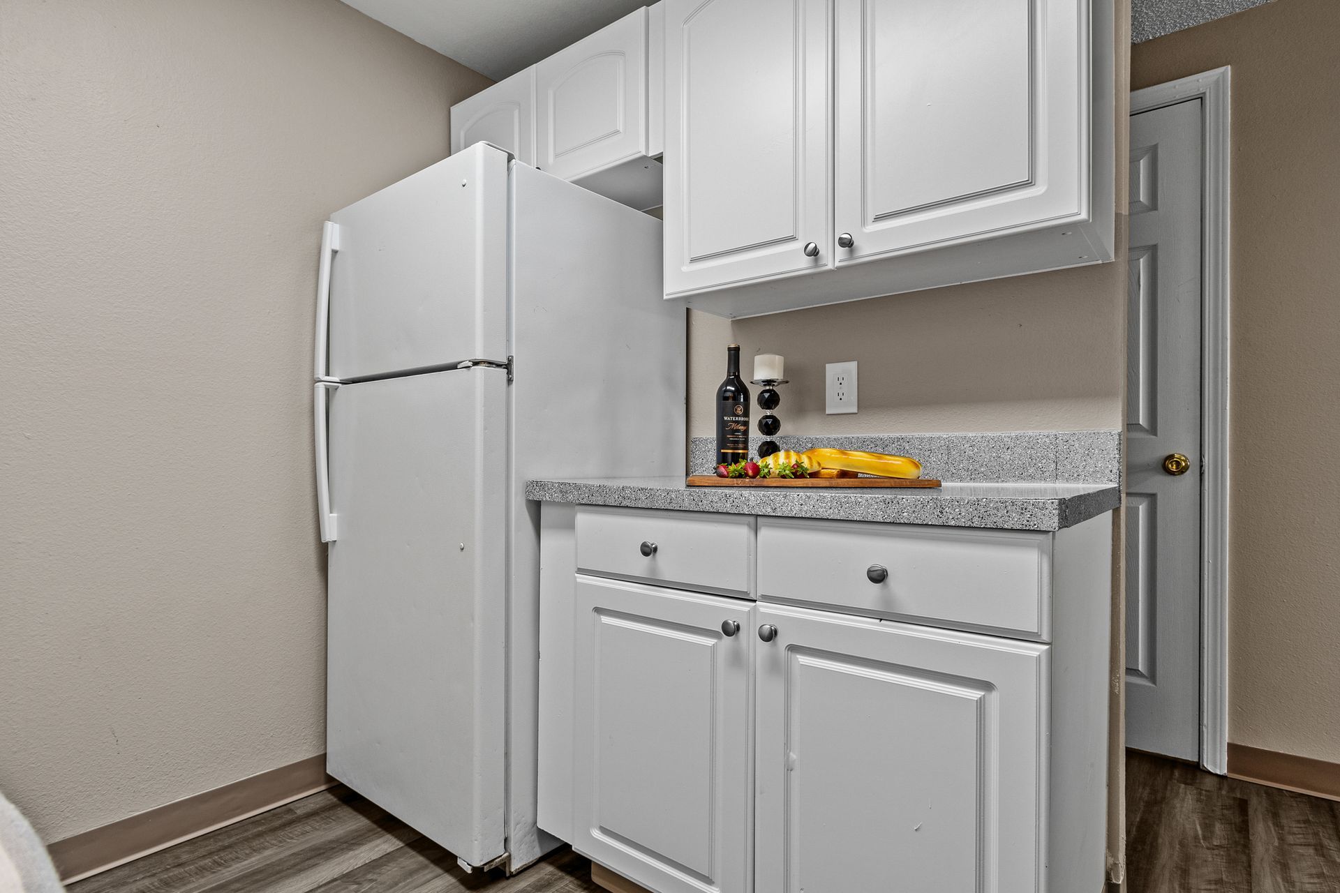 Small kitchen alcove with white refrigerator, cabinets, granite counter, and fruit bowl