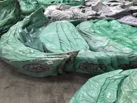 A bunch of green plastic bags are stacked on top of each other on the ground.