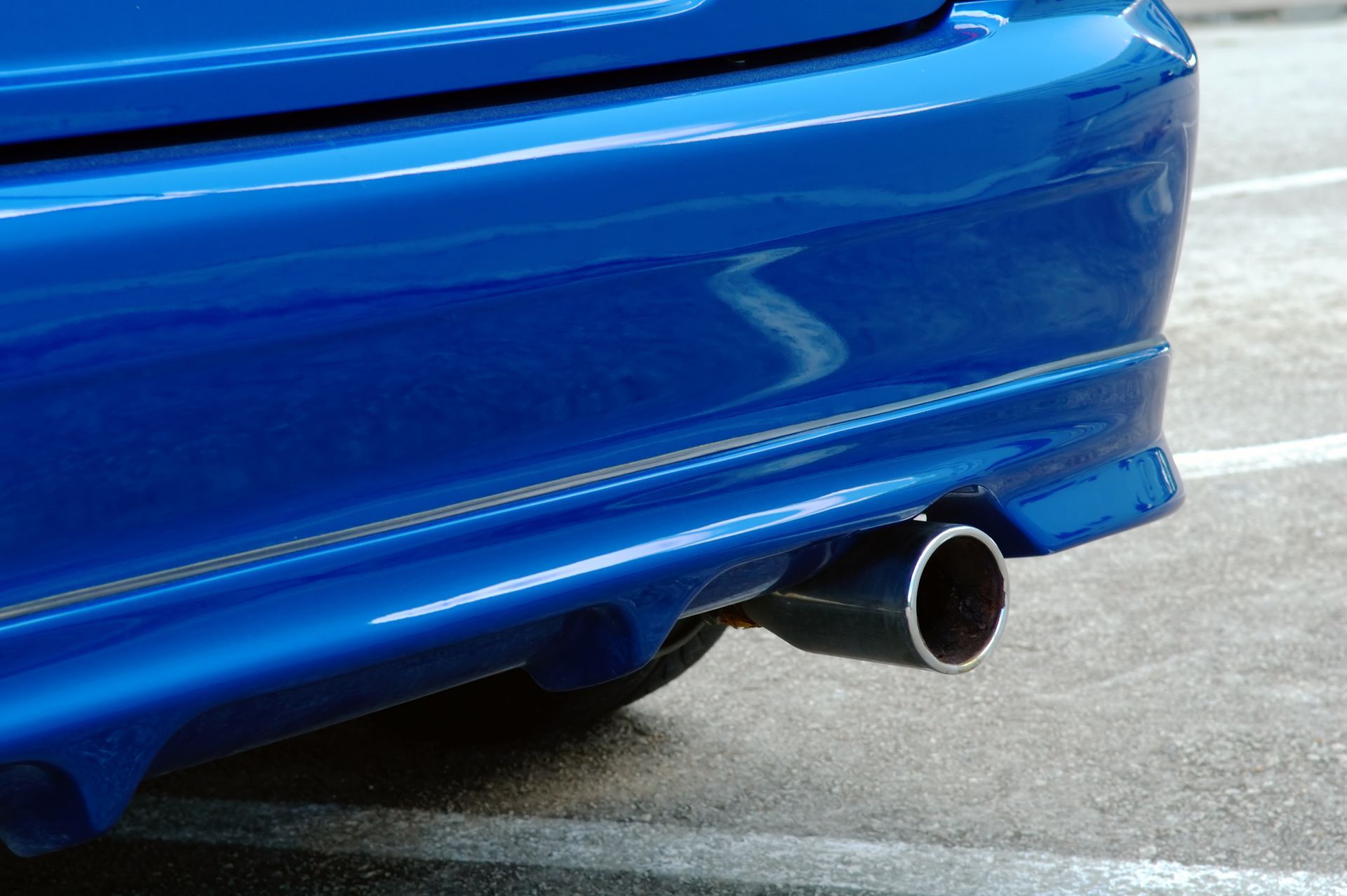 A blue car with a black exhaust pipe is parked in a parking lot.
