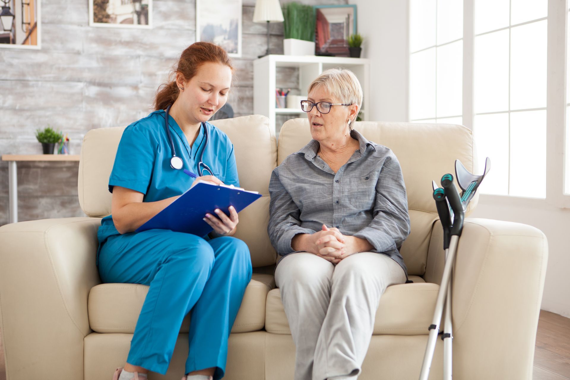 Eine Krankenschwester berät sich mit einer Frau auf einem Sofa und macht sich Notizen.