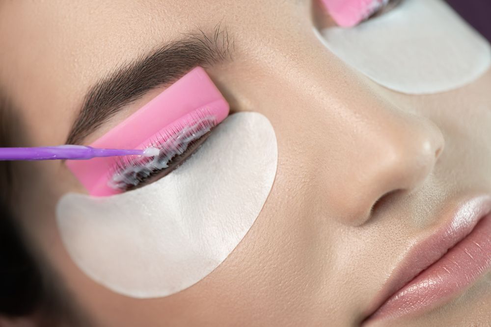 Close-up of eyelash extensions being applied with a purple brush and under-eye pads