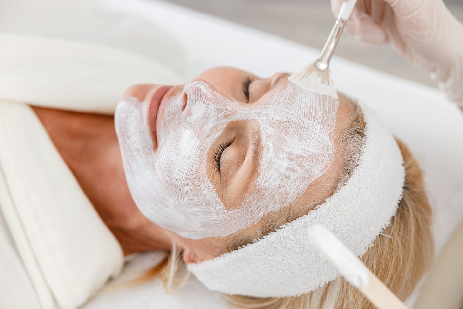 Person receiving a facial mask application with a brush in a spa treatment setting
