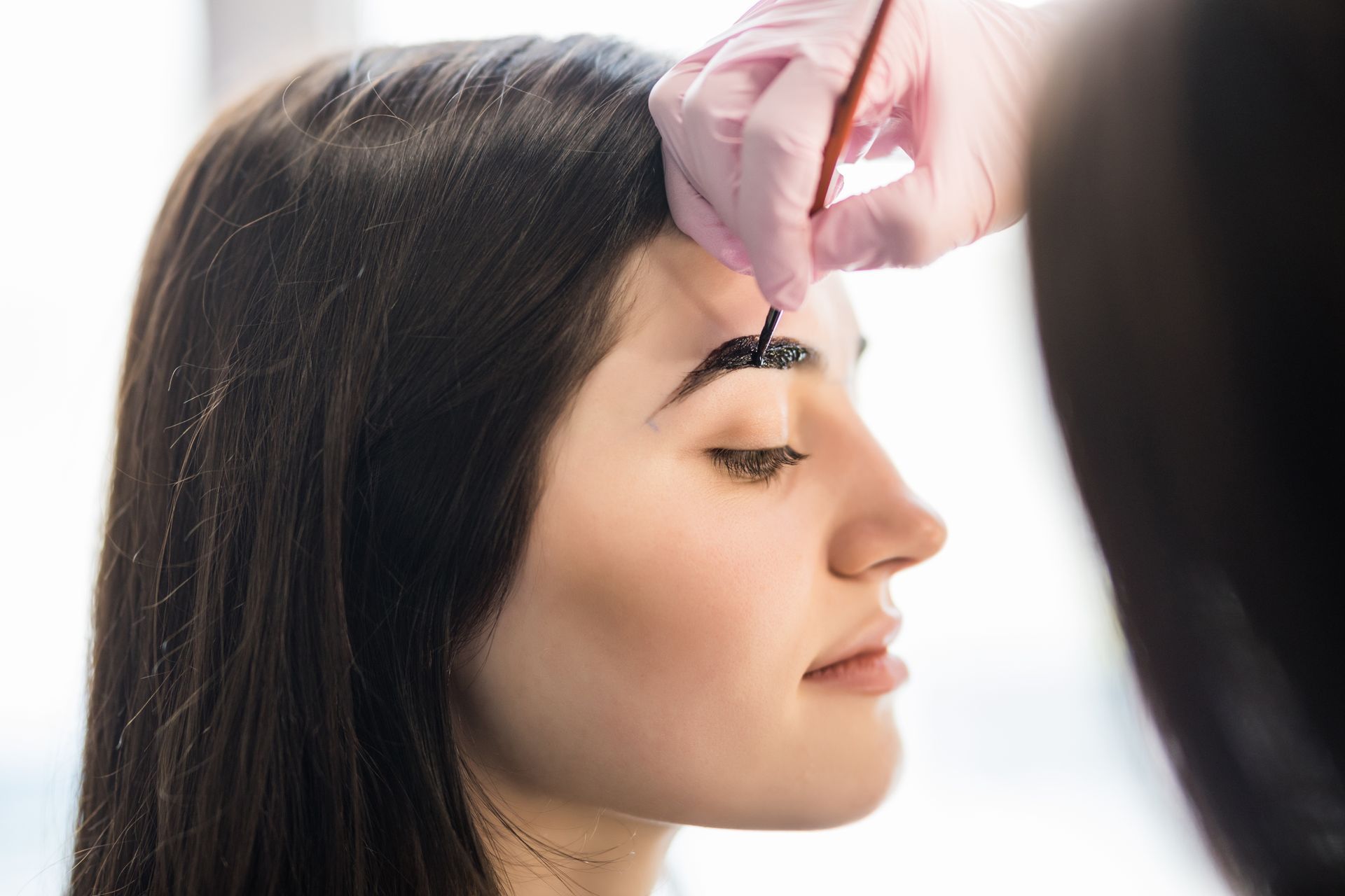 Cosmetologist applying eyebrow makeup to a woman with eyes closed