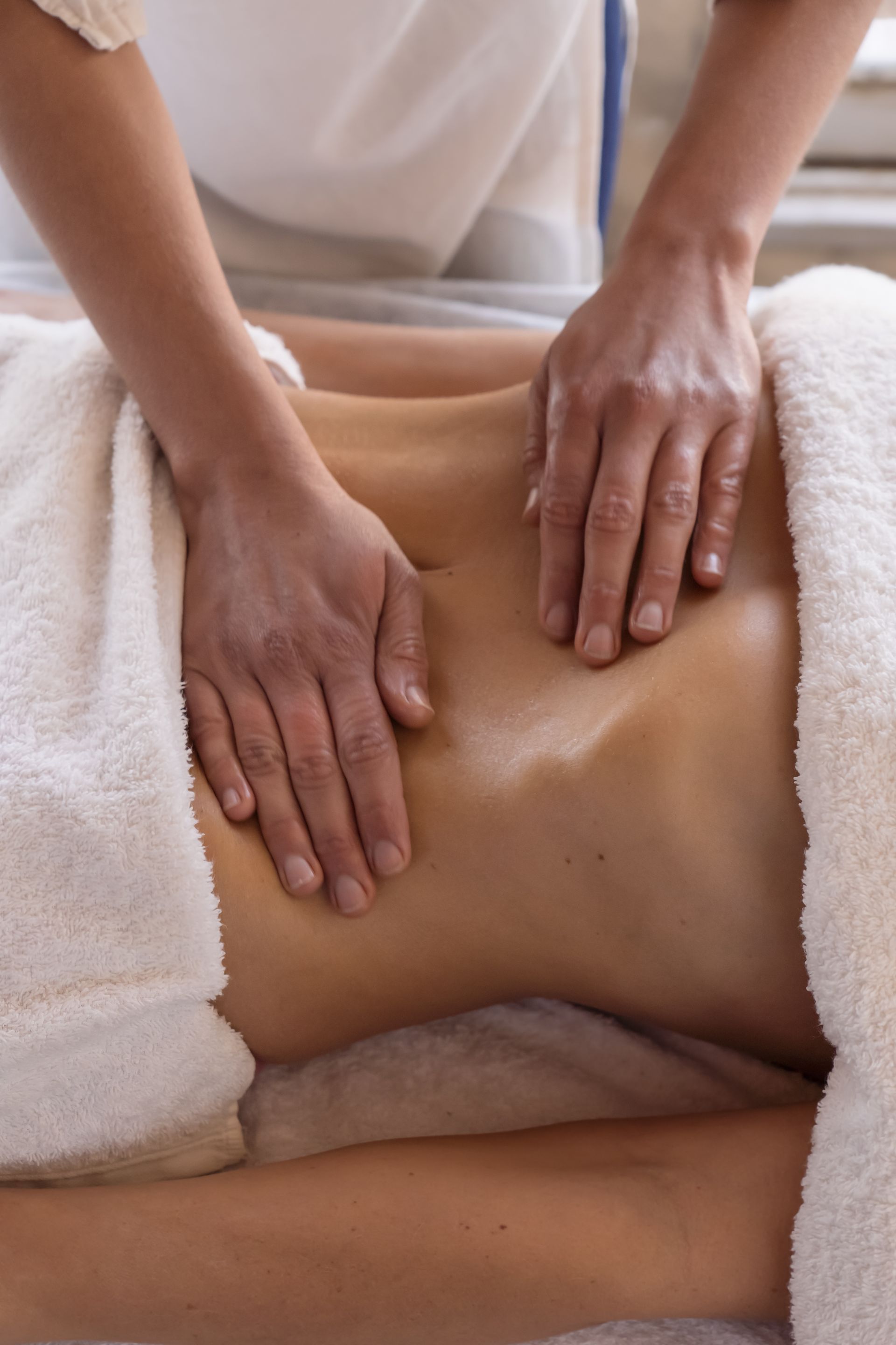 Massage therapist’s hands pressing a client’s bare back on a spa table, with white towels nearby.