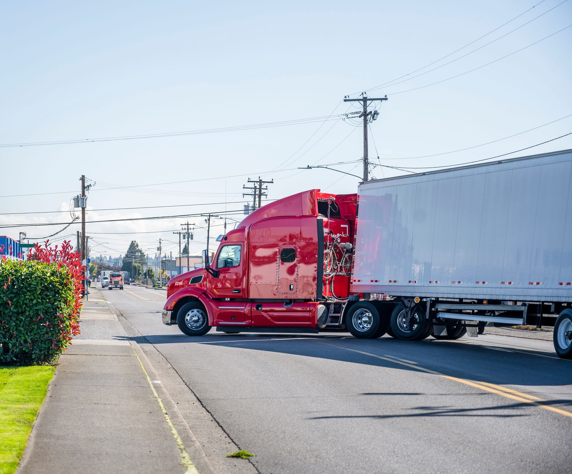 Red semi-truck hauling a white trailer on a sunny suburban street
