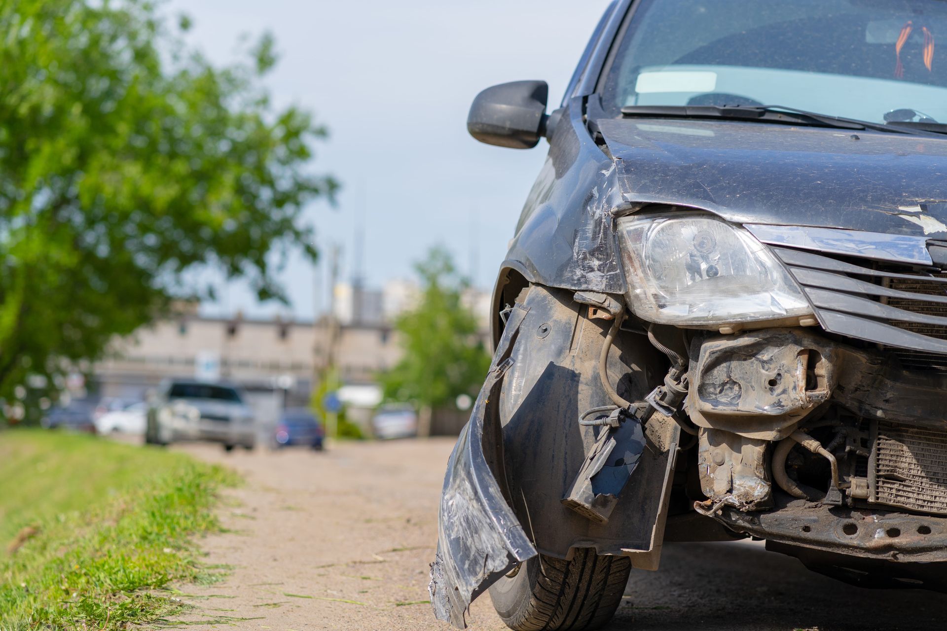Damaged front of a black car after a collision on a roadside, with a detached bumper and debris.