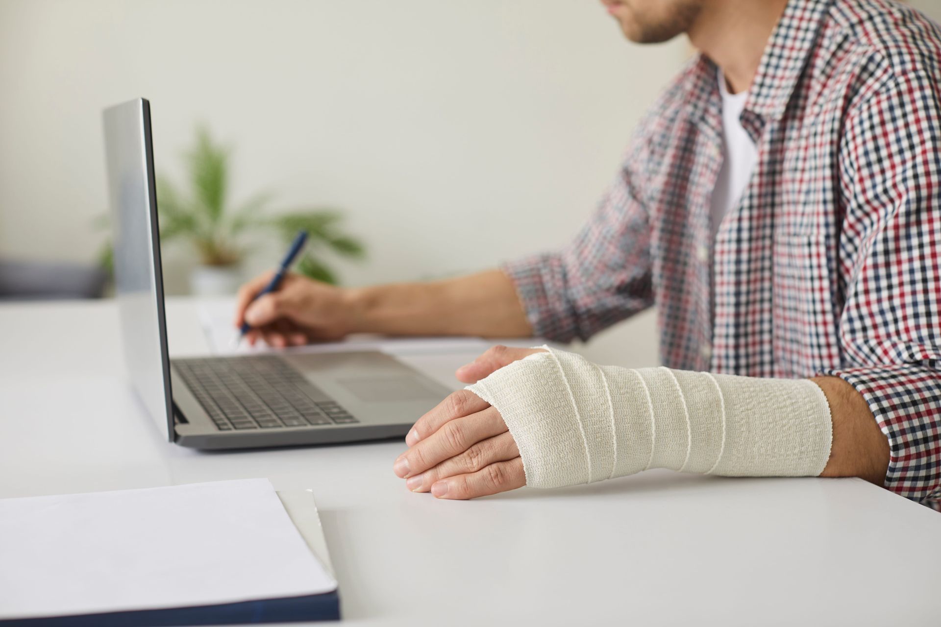 Person with a bandaged hand using a laptop at a desk in a bright office