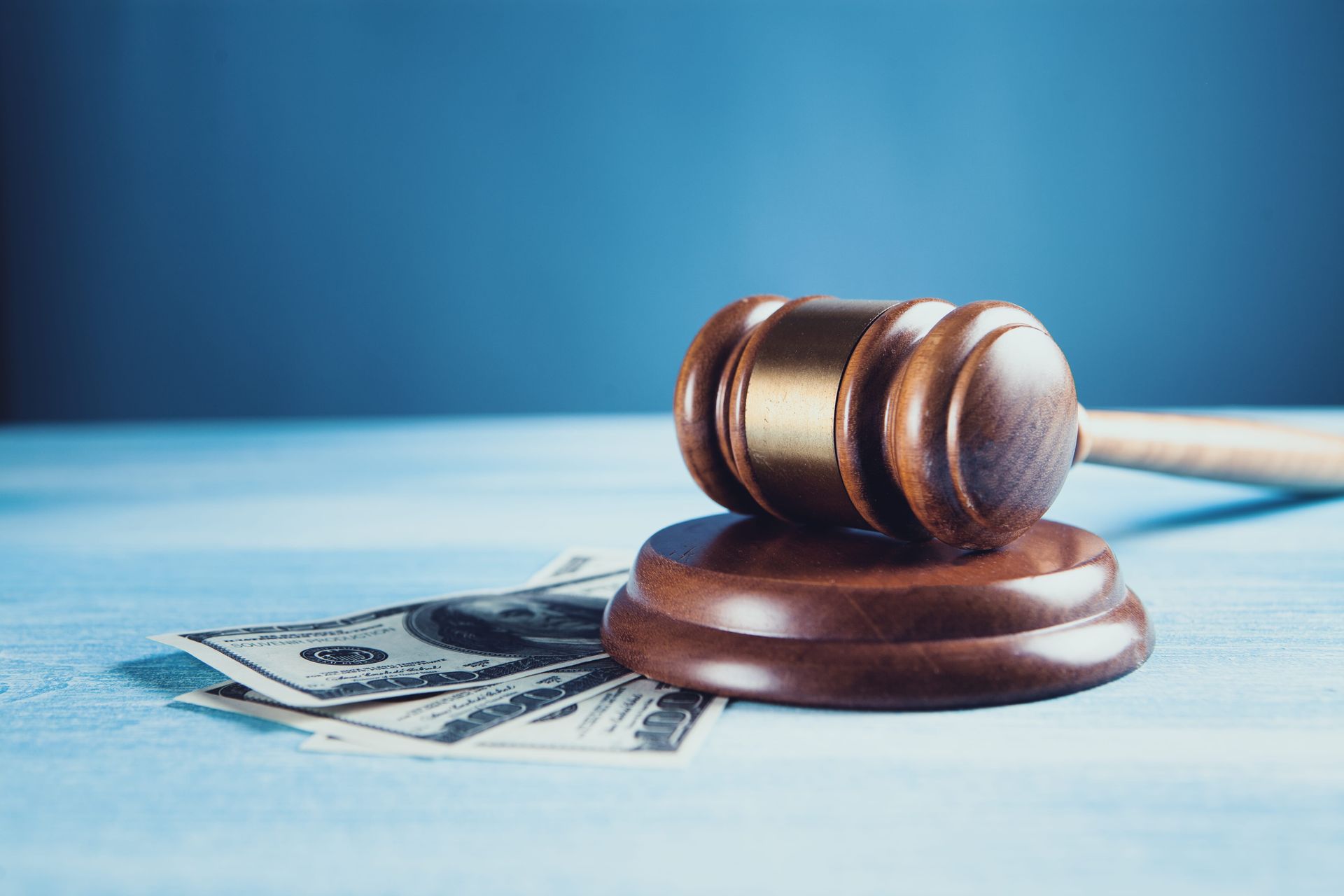 Judge’s gavel resting on a stack of dollar bills against a blue background