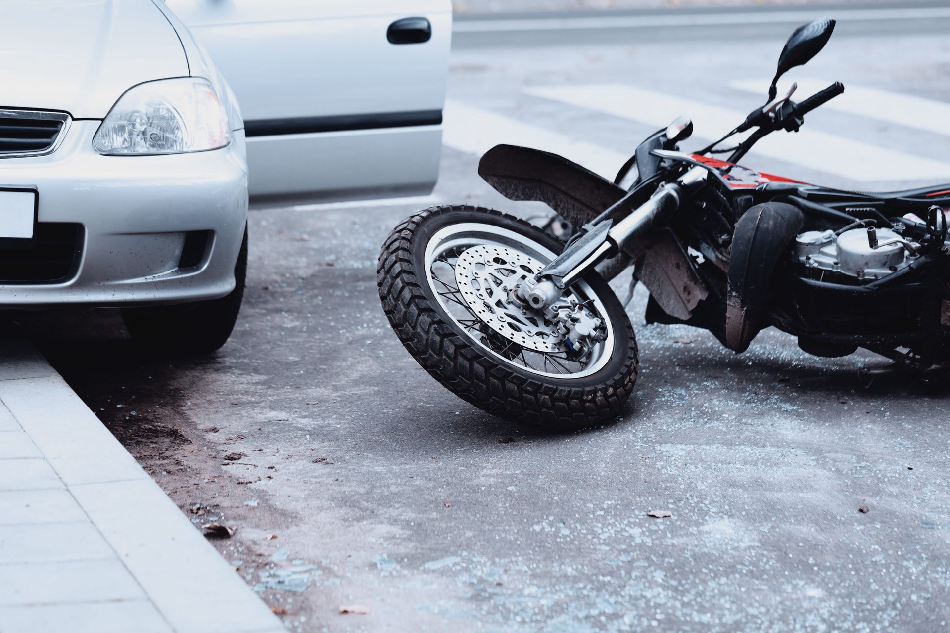 Motorcycle lying on its side after a crash beside a white car on a wet street