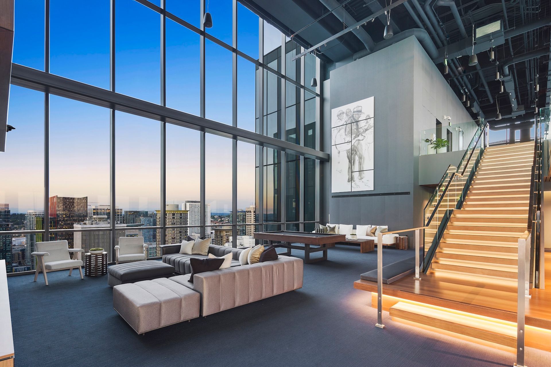 Modern loft office lounge with large windows, staircase, sofas, and city view