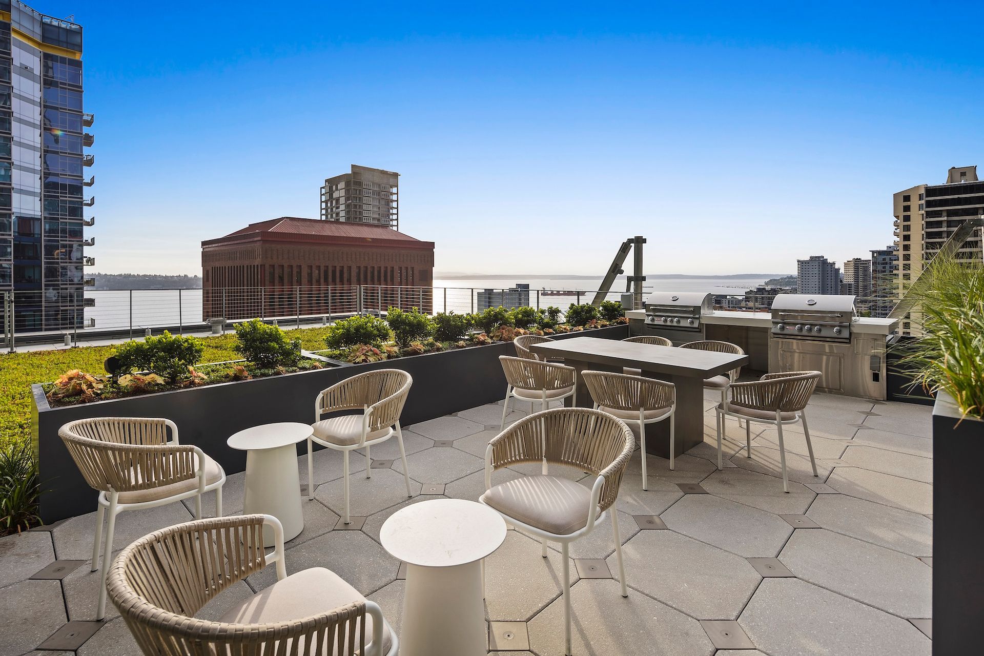 Rooftop patio with wicker chairs, tables, and city skyline under a clear blue sky.