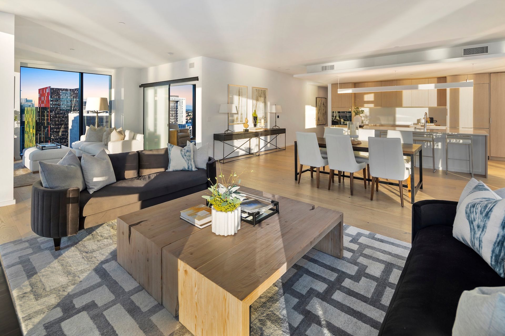 Modern open-concept living room and dining area with gray sofas, coffee table, and bright kitchen beyond.