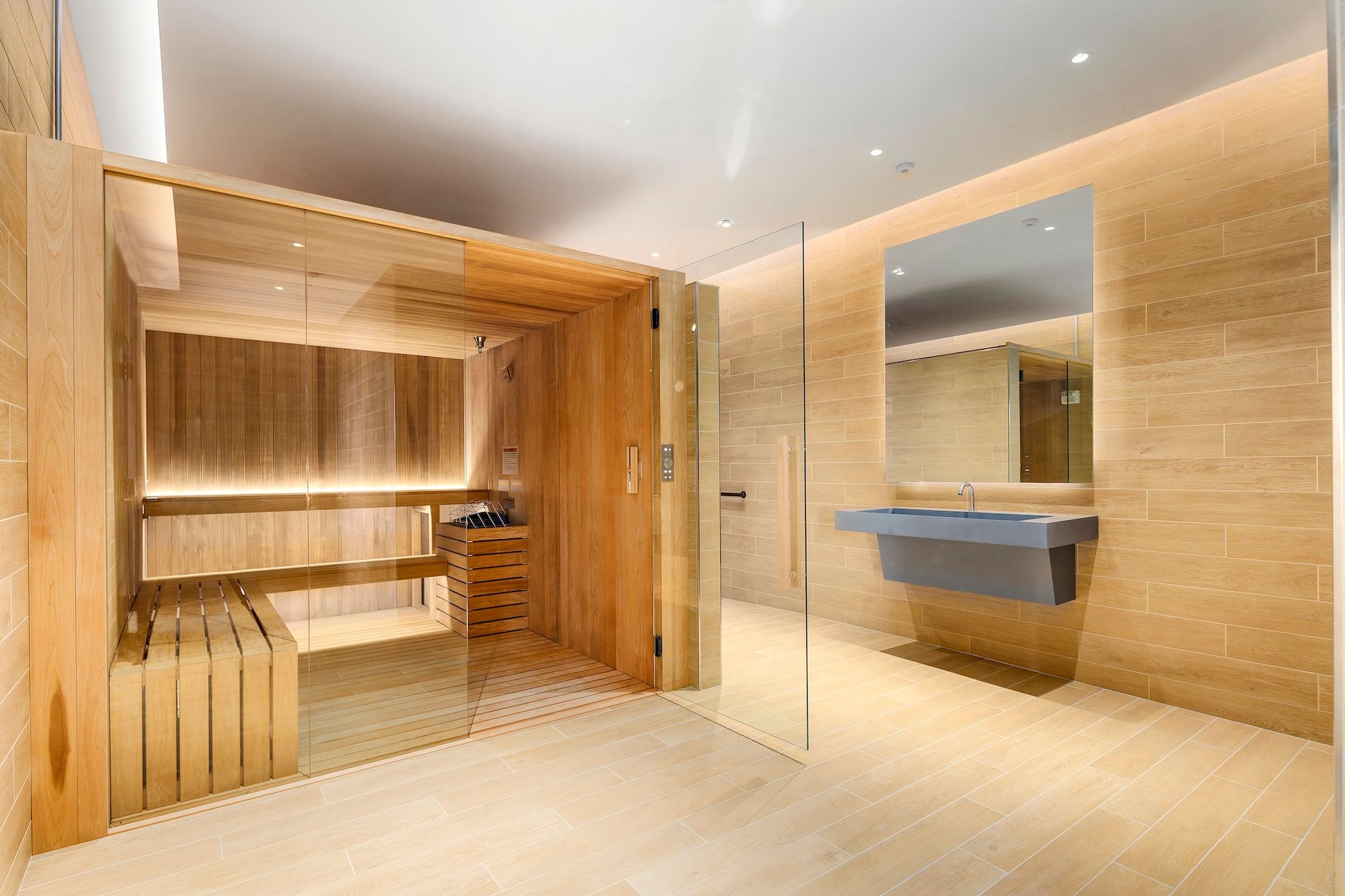 Modern spa interior with warm wood sauna, tiled walls, and a blue sink under a mirror.
