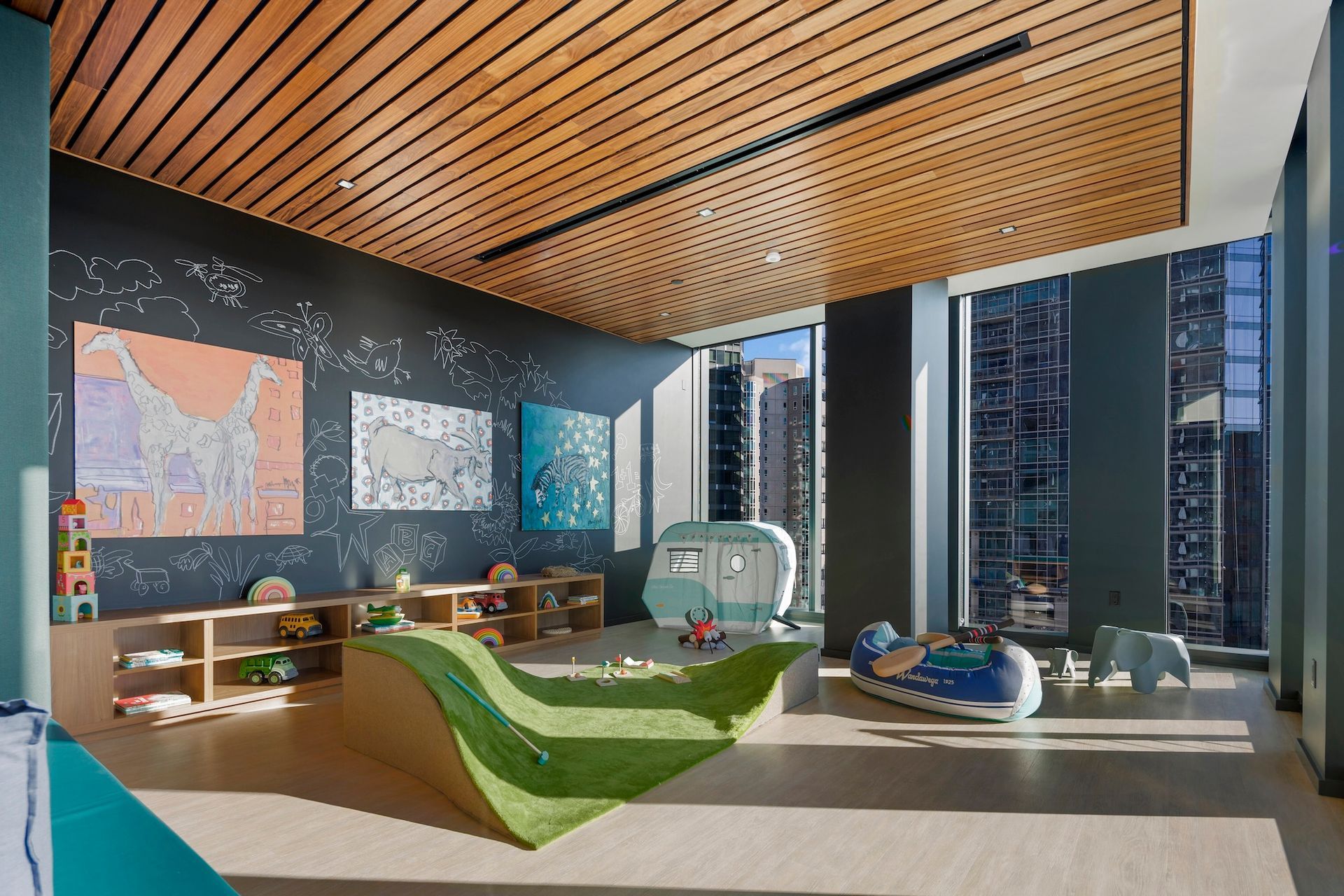 Modern lounge with curved green sofas, wood ceiling, map wall art, and city view through large windows.