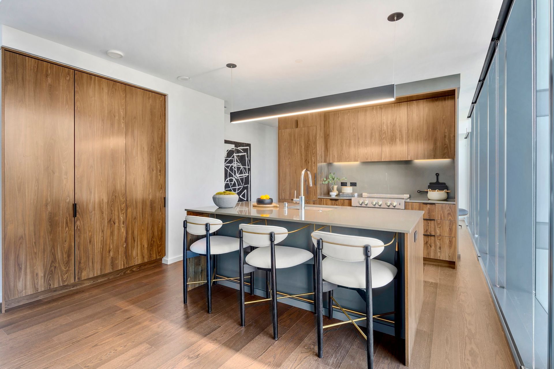 Modern kitchen with island, bar stools, wood cabinets, and blue glass doors.