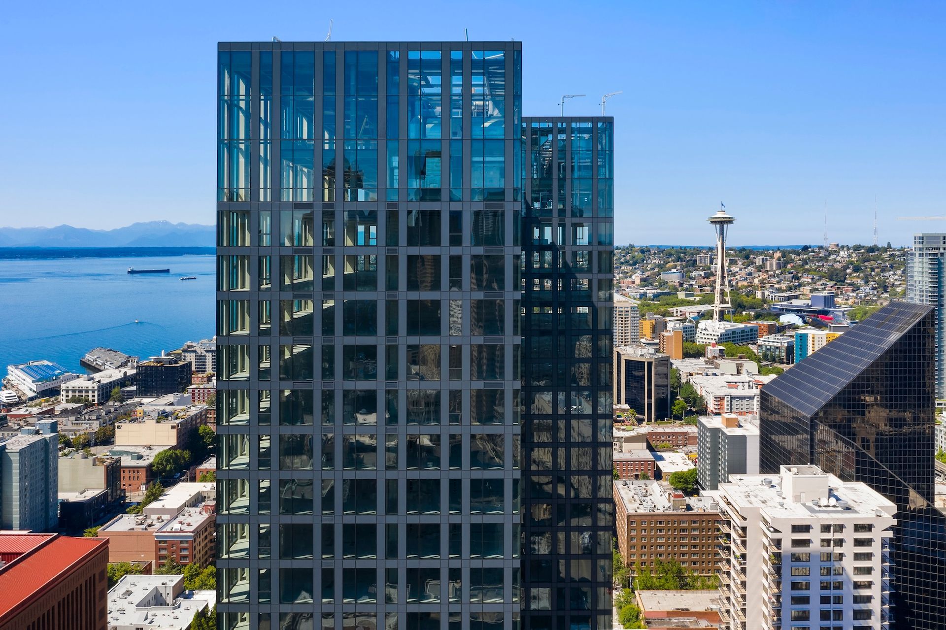 Tall glass high-rise overlooking a waterfront city and harbor under a clear blue sky