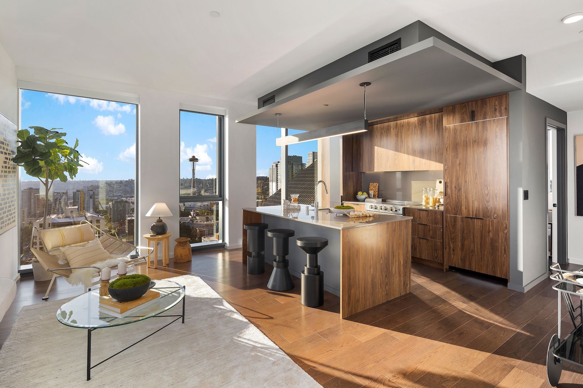 Modern loft kitchen and living room with wood accents, bar stools, and city view through floor-to-ceiling windows.